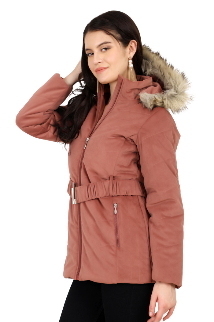 A woman in a side pose showcases the minimalist design of Coatsnmore’s onion pink velvet quilted jacket, featuring stand collar, removable hood, waistband zip closure, concealed zippered side pockets, and black jeans with her right hand on her hair.